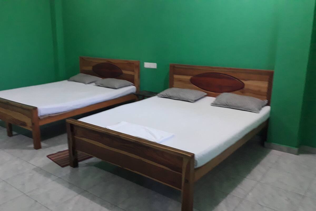 Two wooden beds with white linens in a room with green walls and a tiled floor.