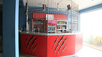 Un mostrador rojo con estructura de metal tipo jaula, estantes con botellas y una persona al fondo.