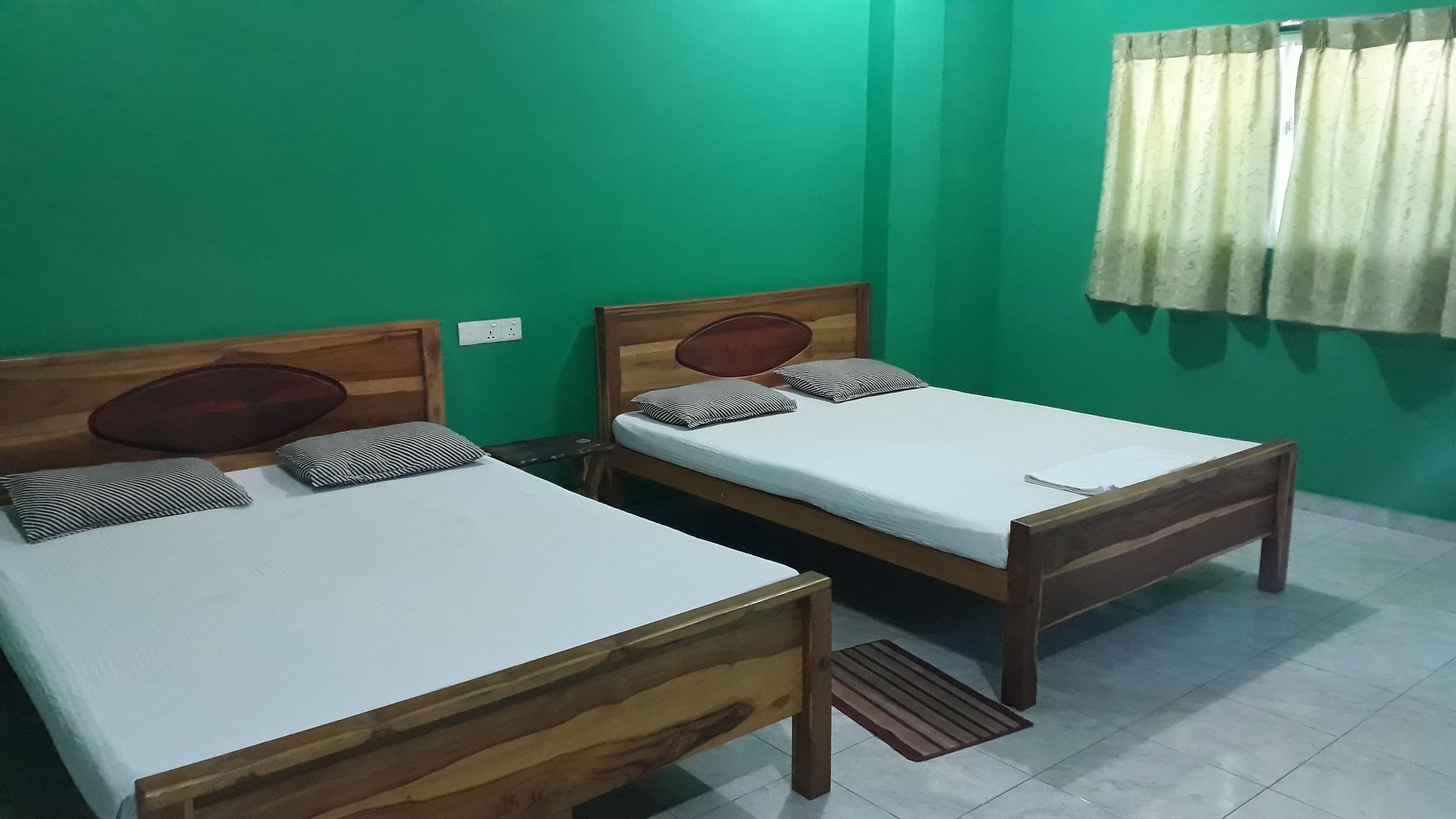 Two wooden beds with white linens and striped pillows in a room with green walls and a window with curtains.