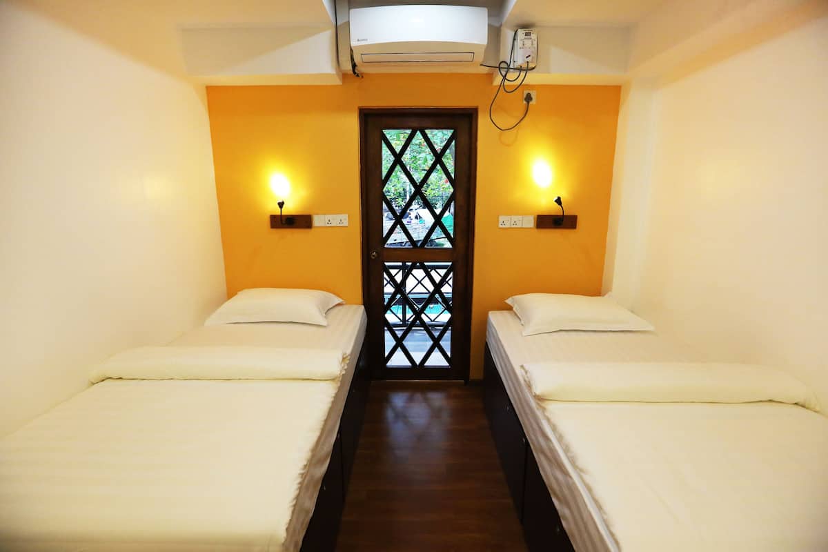 Una habitación con dos camas individuales, suelo de madera, ventana con diseño de celosía e iluminación en la pared.