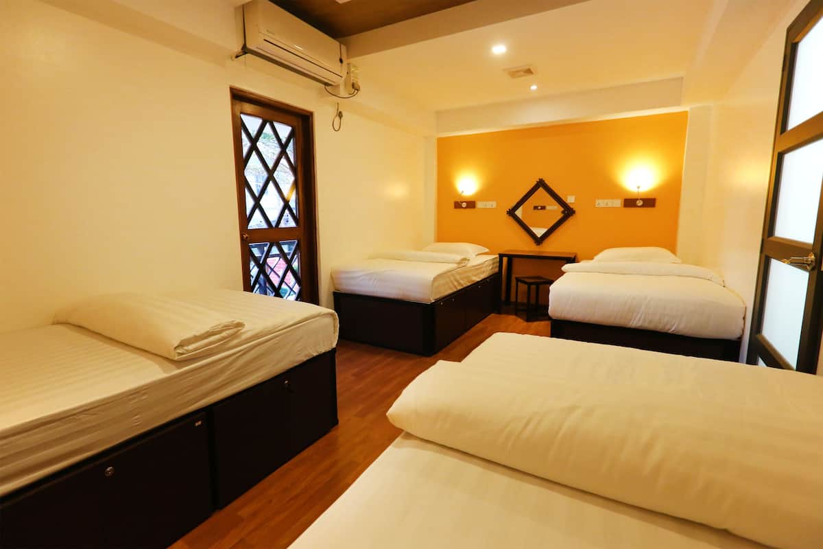 Habitación de hotel con tres camas, suelo de madera, una mesita y una ventana con celosía.
