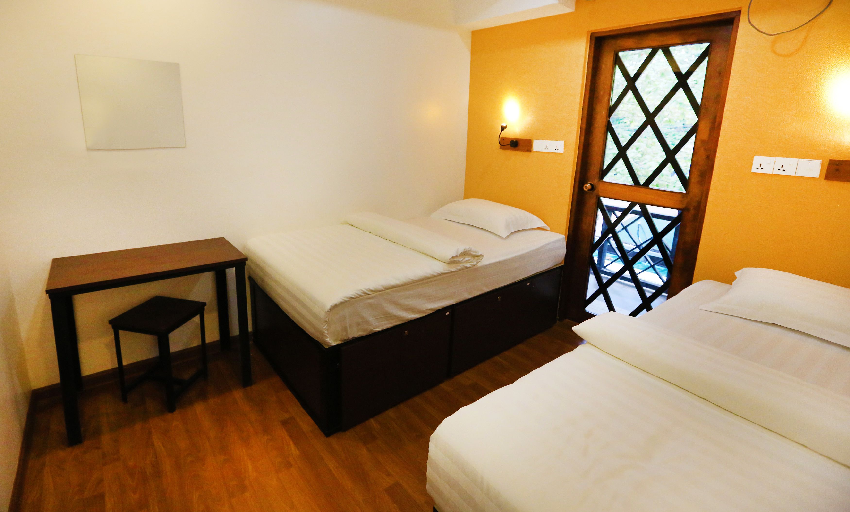 Une chambre avec deux lits, une petite table et une porte en bois ornée d’un motif en treillis.