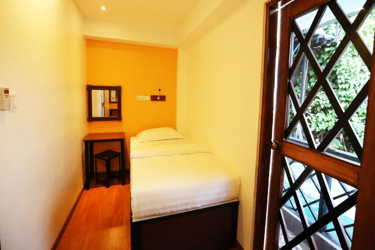Una habitación pequeña y luminosa con una cama, una mesita de noche, un espejo y una ventana con un diseño de celosía.