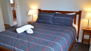 A neatly made bed with a plaid bedspread, two bedside lamps, and a folded towel on the bed. - Freycinet Sands (Coles Bay)