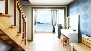 Ein Zimmer mit einer Holztreppe, einem Schreibtisch mit Spiegel und Blick auf das Meer durch eine große Schiebetür.