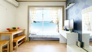 Ein Zimmer mit einem Bett, einer Holzbank, einem kleinen Tisch mit Korb und Gläsern, einem Fernseher und einem Fenster mit Vorhängen.