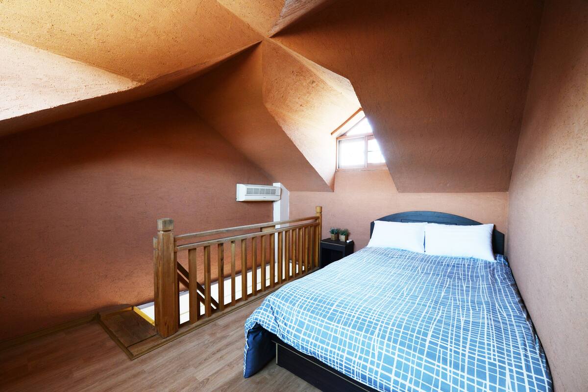 A bedroom with a wooden bed, a small bedside table, a nightstand, and a window with a view.