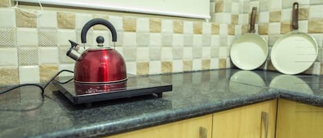 A kitchen with a red kettle on a black induction cooktop, wooden cabinets, and a tiled backsplash.