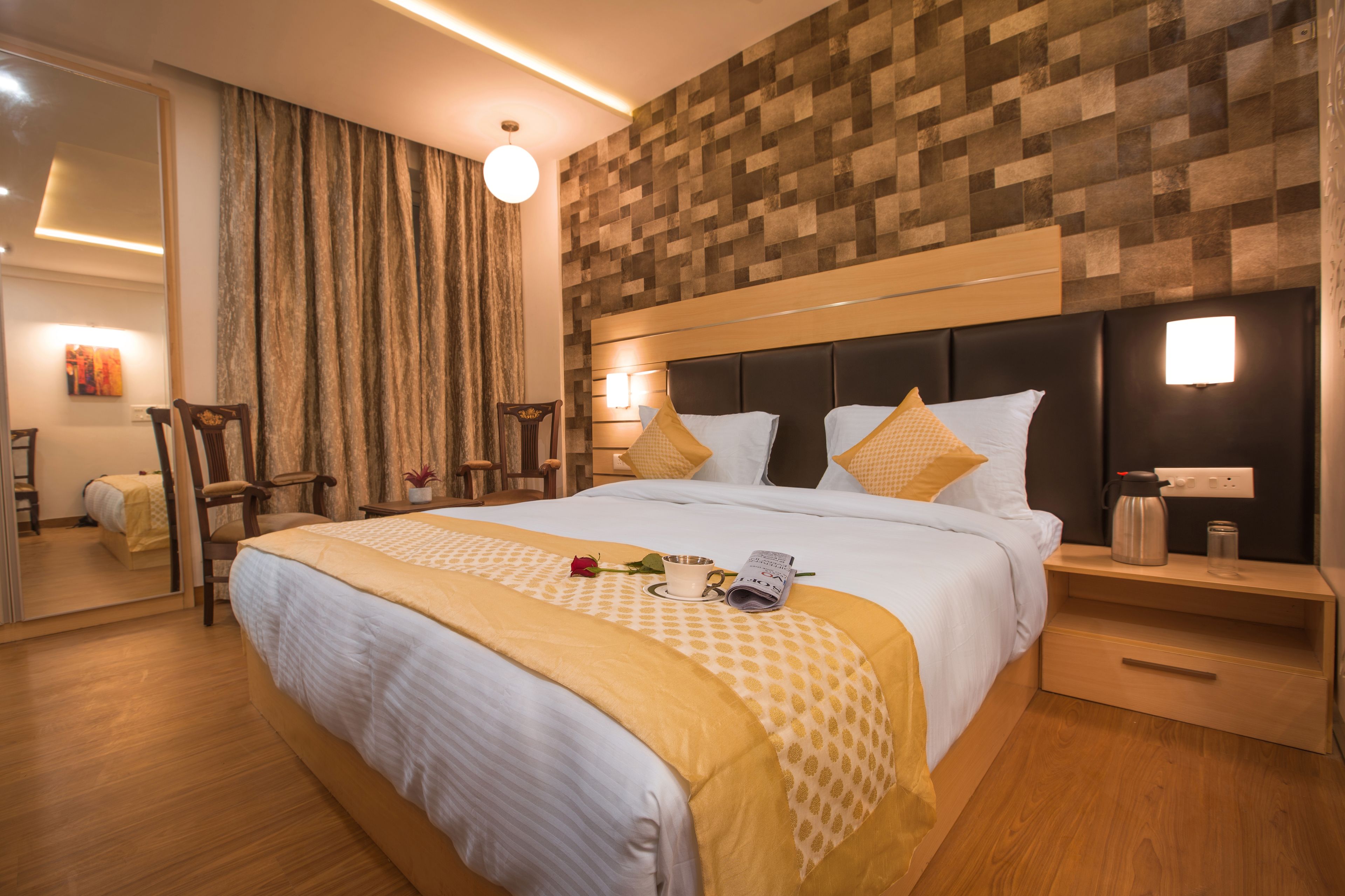 Una habitación de hotel con una cama grande, cabecero de madera, una mesita de noche con lámpara y un espejo.