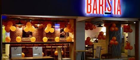 Un restaurant sur le thème des cafés, avec un panneau au néon, des tables, des chaises et des ballons.