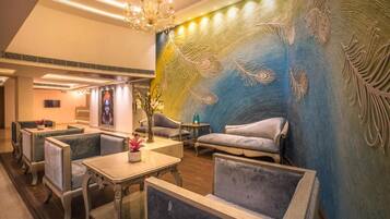 A hotel lobby with seating areas, a chandelier, and a wall with feather patterns.