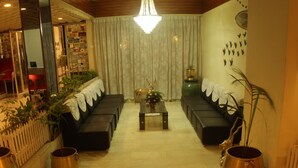 A living room with a chandelier, sofas, a coffee table, and potted plants. - Hotel Parisutham (Thanjavur)
