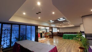 A spacious room with a high ceiling, recessed lighting, and a large window with a geometric screen. - Hotel Parisutham (Thanjavur)