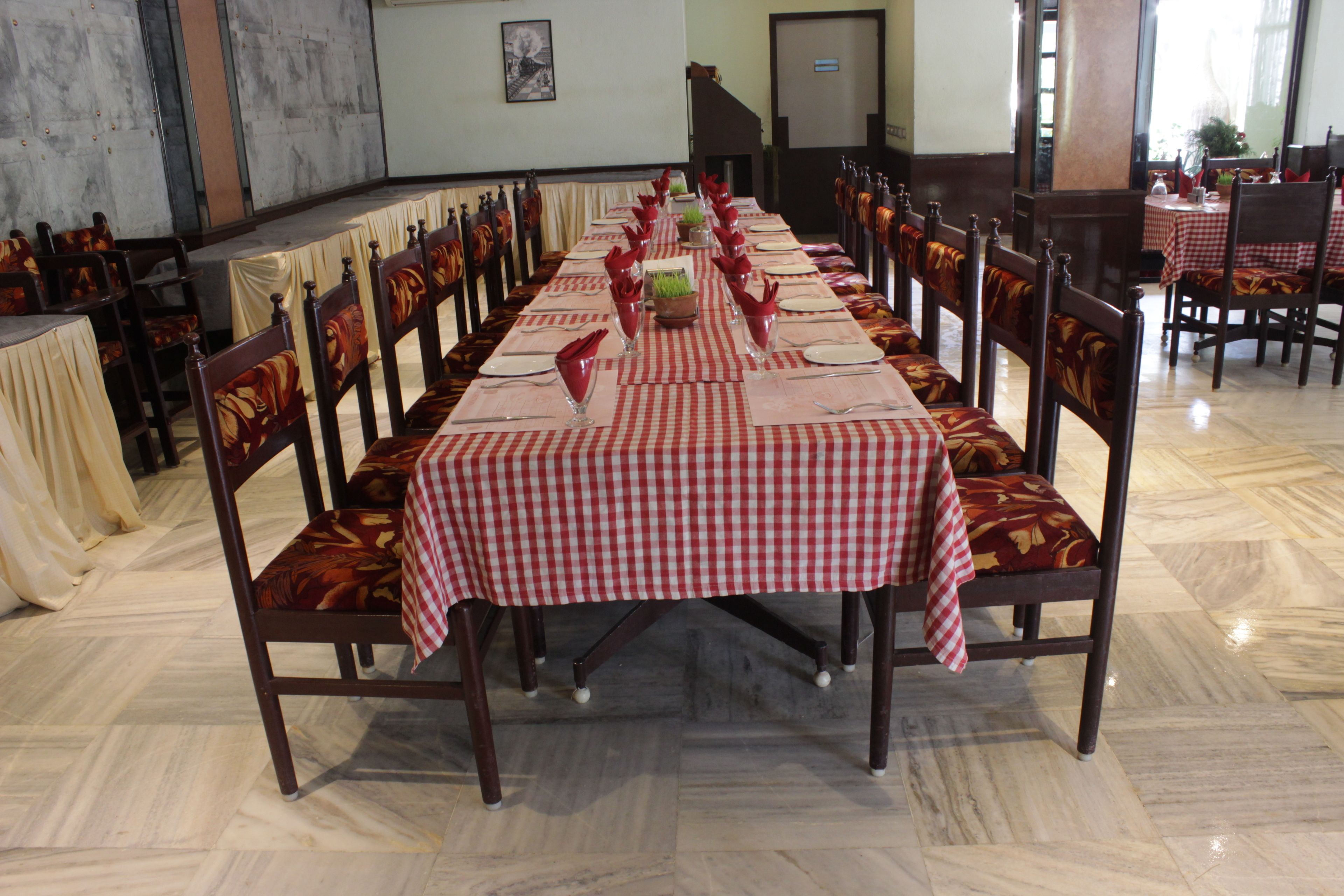 A long dining table set with red and white checkered tablecloths, surrounded by wooden chairs with floral upholstery.