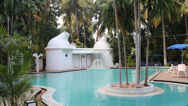 A swimming pool with a circular design, surrounded by palm trees and a white structure with a unique shape. - Hotel Parisutham (Thanjavur)