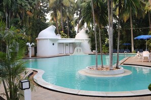 A swimming pool with a circular design, surrounded by palm trees and a white structure with a unique shape. - Hotel Parisutham (Thanjavur)