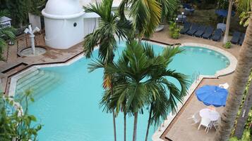 Relax by the serene pool surrounded by lush greenery and palm trees, with lounge chairs and umbrellas for a comfortable retreat.