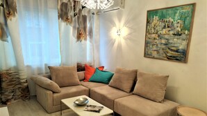 A living room with a beige sectional sofa, a coffee table, and a side table. There is a painting on the wall and a chandelier. - Baratero City I Apartment (Sofia)