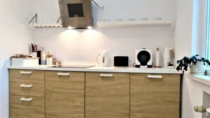 A modern kitchen with wooden cabinets, a built-in range hood, a kettle, a coffee maker, and a tablet on the counter. - Baratero City I Apartment (Sofia)