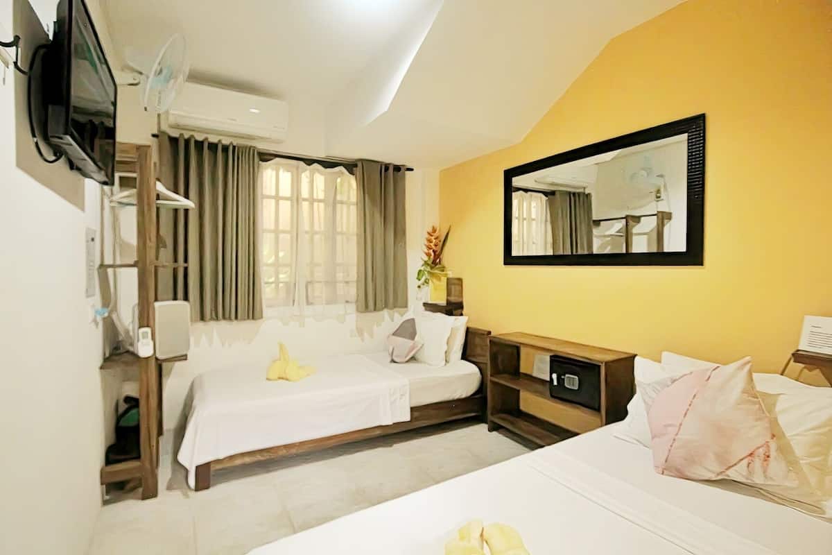 Una habitación de hotel con cama, mesita de noche, espejo, televisor y ventana con cortinas.