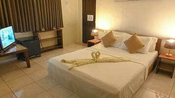 A hotel room with a neatly made bed, a television on a desk, and a lamp on the bedside table.