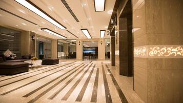 Een ruime lobby met een modern design, met een groot zitgedeelte met banken en een salontafel, een patroon vloer en een receptiebalie.