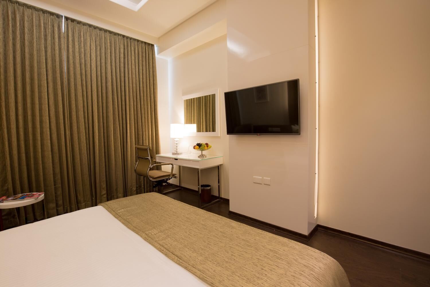 A hotel room with a bed, a desk with a lamp, a chair, a TV, and a window with curtains.