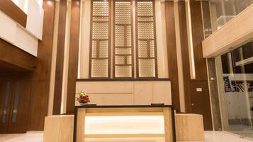 A reception desk with a wooden finish, a glass partition with a geometric pattern, and a small flower arrangement.