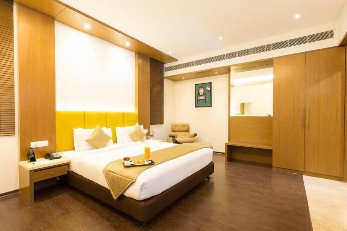 A hotel room with a bed, bedside table, chair, and a large mirror.