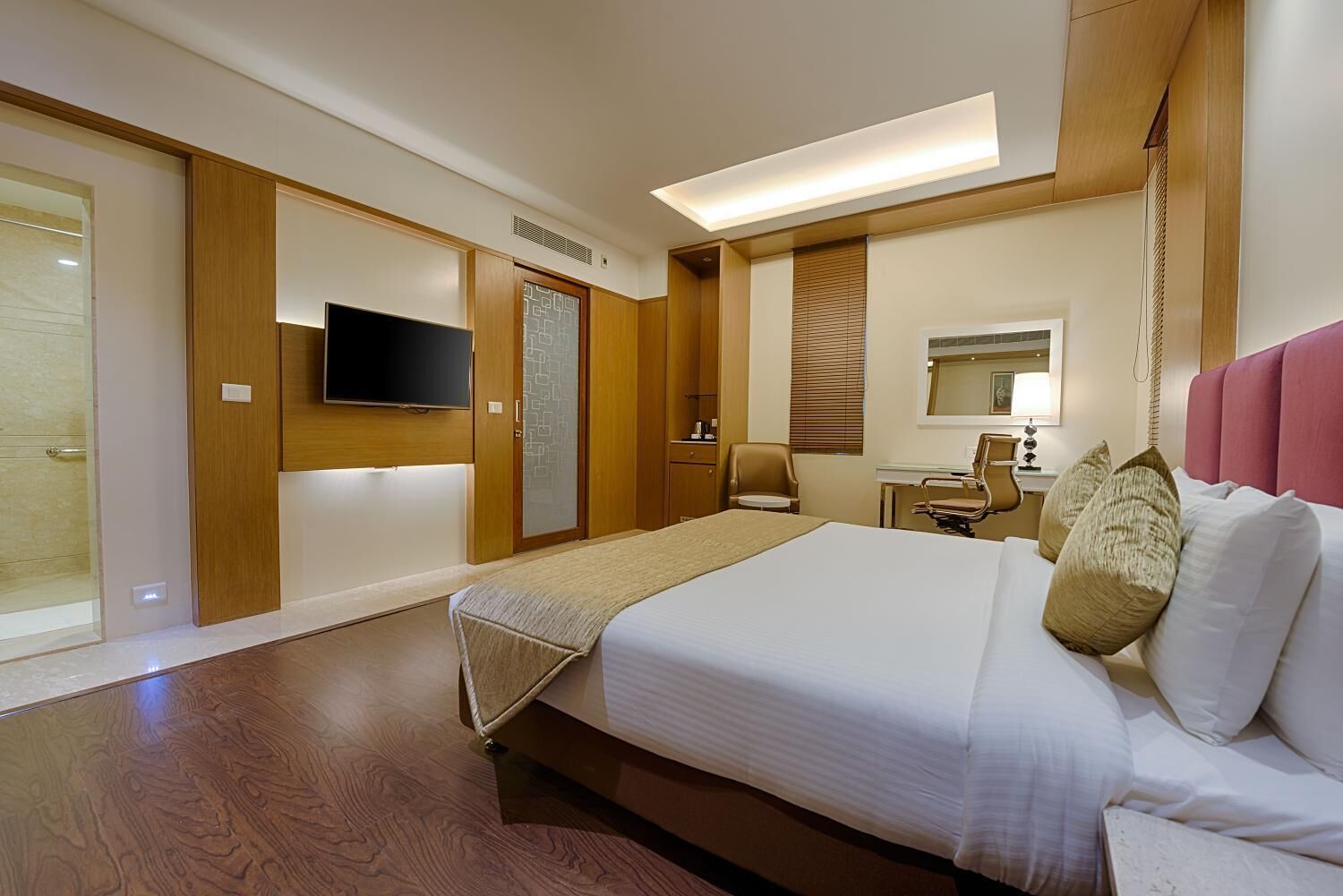 A hotel room with a large bed, a desk, a chair, a television, and a sliding door.