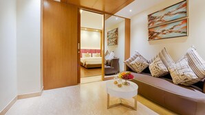A modern hotel room with a sofa, a small round table with a fruit bowl, and a bed with a pink headboard. - Hotel Kiscol Grands (Coimbatore)