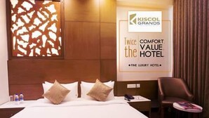 A hotel room with a bed, pillows, a nightstand, a chair, and a wall-mounted sign advertising the hotel. - Hotel Kiscol Grands (Coimbatore)