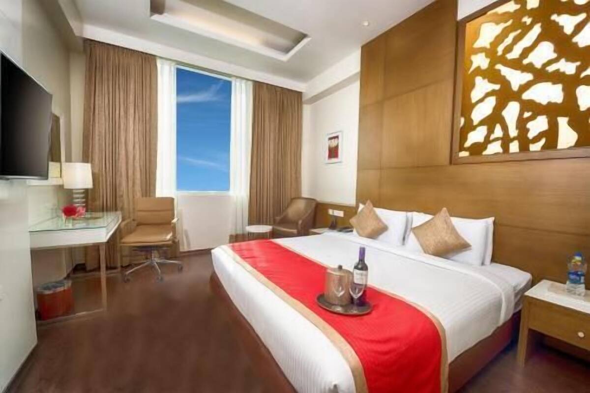 A hotel room with a bed, a desk, a chair, a TV, and a window.