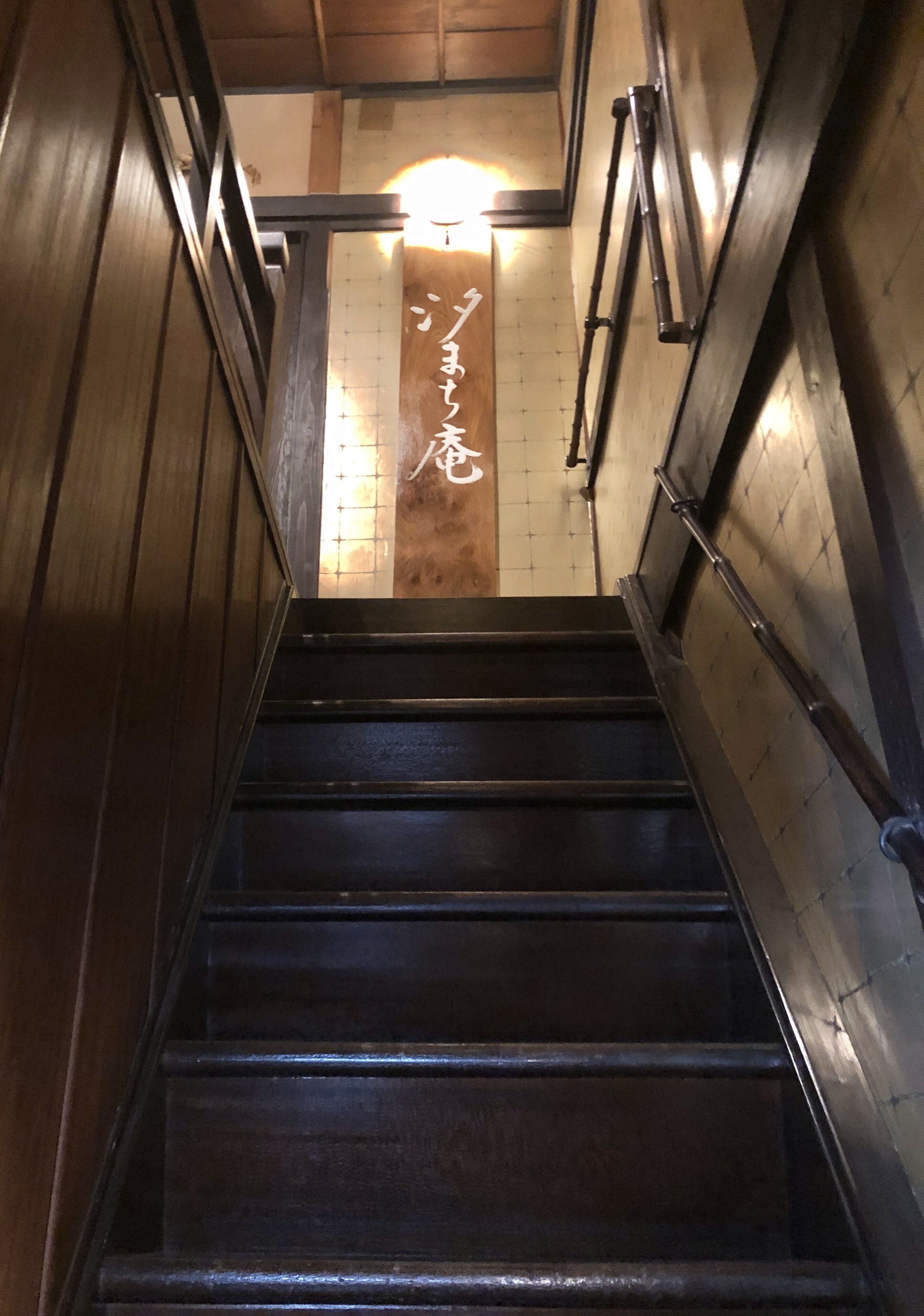 Una escalera de madera con barandillas metálicas y un panel de madera con caracteres japoneses.