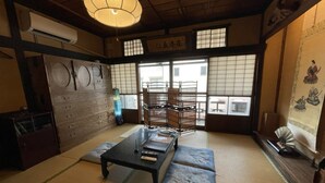 Ein traditioneller japanischer Raum mit Tatami-Boden, einem niedrigen Tisch mit Kissen, einer hängenden Leuchte und einer Schiebetür mit Blick ins Freie.