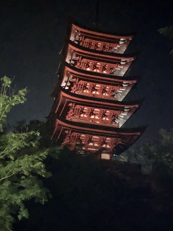 Un bâtiment à plusieurs étages, de style pagode, dont les niveaux supérieurs sont illuminés, et qui est entouré de verdure.