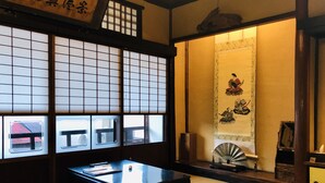 Ein traditioneller japanischer Raum mit Tatami-Böden, einem niedrigen Tisch, Kissen, Shoji-Bildschirmen und einer Schiebetür.