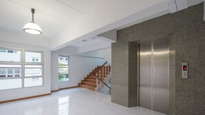 A spacious lobby with a modern elevator, a staircase, and large windows allowing natural light. - JR Mansion (Bangkok)