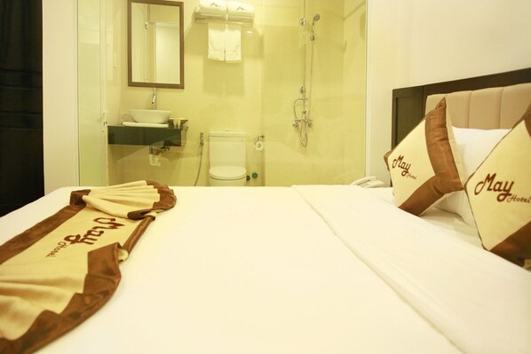 A hotel room with a bed, a bathroom with a glass shower enclosure, and a bedside table with a phone. - May Hotel (Da Nang)