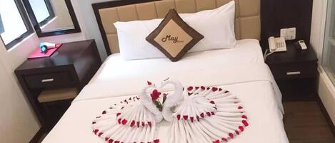 A hotel room with a bed, a nightstand, a bedside table, and a window.