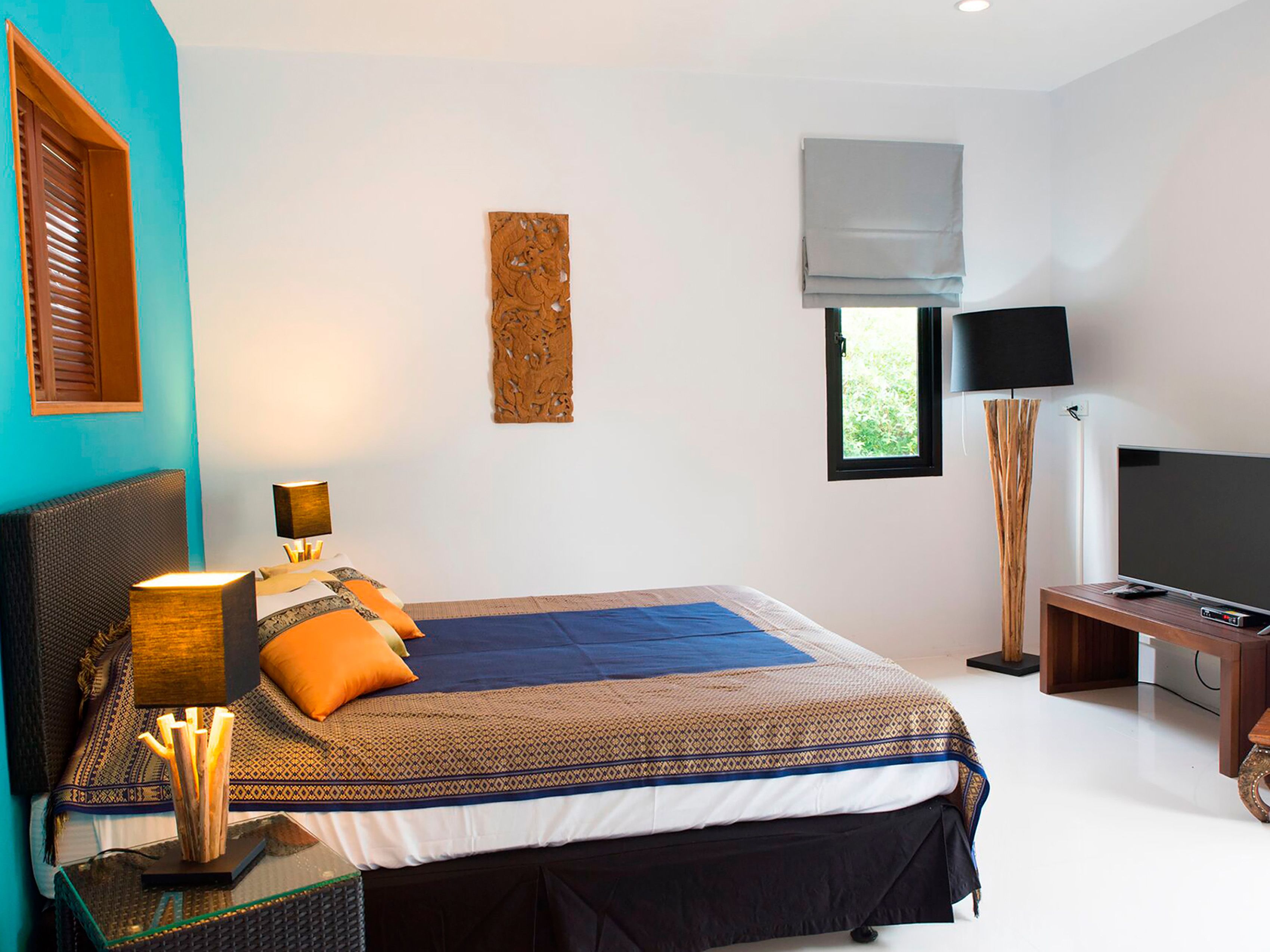 A bedroom with a bed, bedside table, lamp, and a TV.