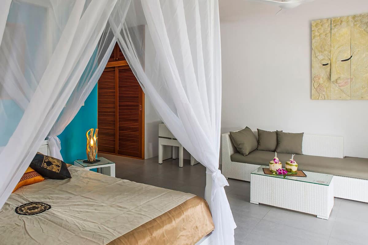 A bedroom with a bed, a nightstand, a bedside table, a sofa, a coffee table, and a wall with a painting.