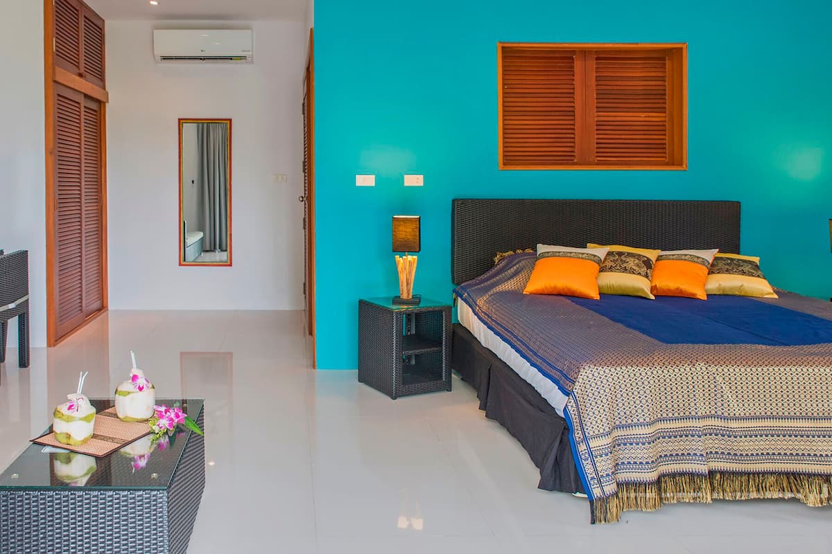 A bedroom with a bed, a nightstand, a mirror, and a window with wooden shutters.
