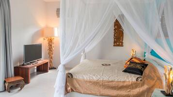 Een slaapkamer met een hemelbed, een televisie op een houten standaard, een nachtkastje en een decoratief item aan de muur.