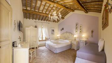 A bedroom with a large bed, a smaller bed, a desk with a lamp, a chair, and a chandelier.