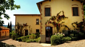 A two-story building with a yellow facade, arched windows, and a garden with various plants and flowers. - Agriturismo Il Segreto di Pietrafitta (San Gimignano)