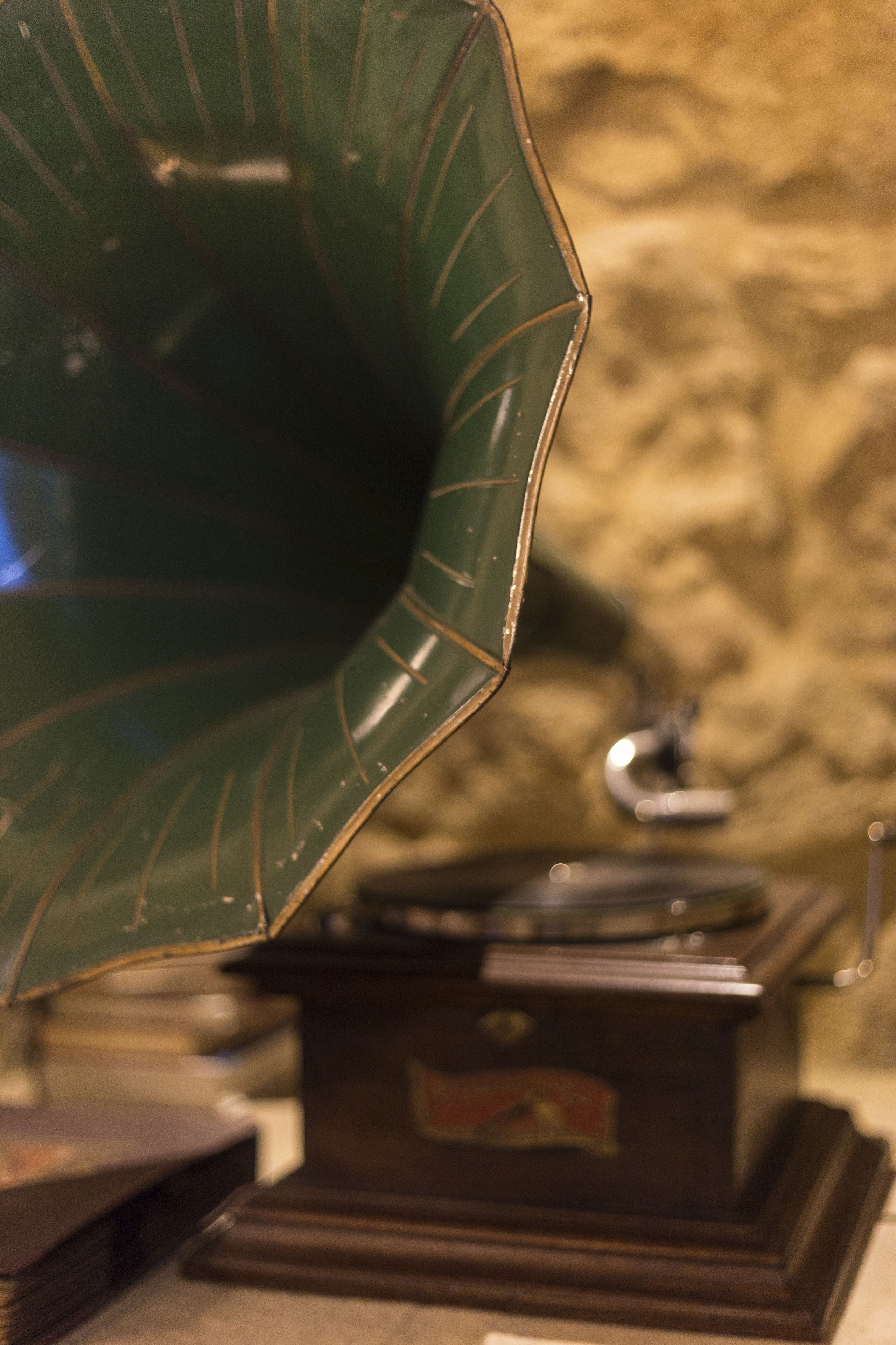 Un giradischi d'epoca con un corno verde e una base in legno, posizionato su un tavolo davanti a una parete strutturata.