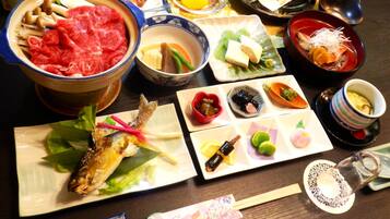 A variety of Japanese dishes including a bowl of raw beef, a fish on a leaf, and several small plates with pickles and vegetables.