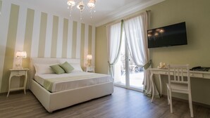 Una habitació amb llit, taules de nit, escriptori, cadira, televisió i finestra amb cortines.