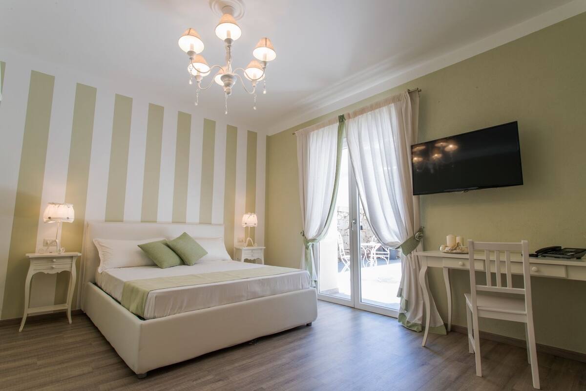 A bedroom with a bed, bedside tables, a desk, a chair, a TV, and a window with curtains.